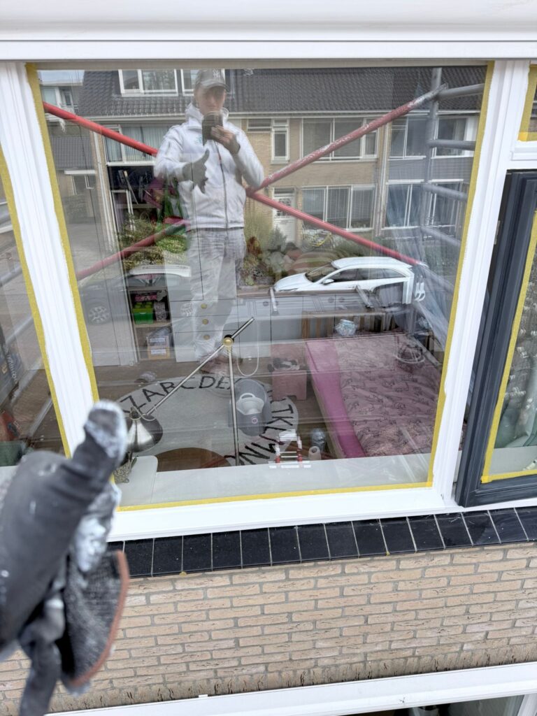 Buiten schilder schildert kozijn en raam.