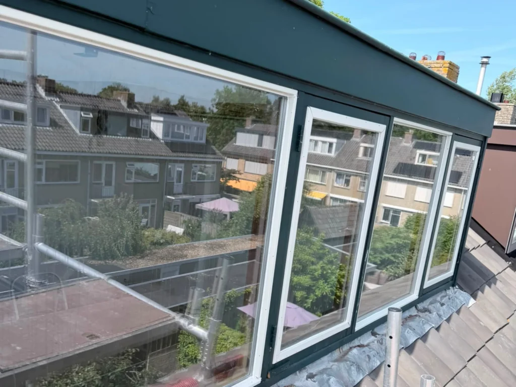 Brede donkergroene dakkapel met nieuwe beglazing in witte glaslatten op een pannendak in Castricum