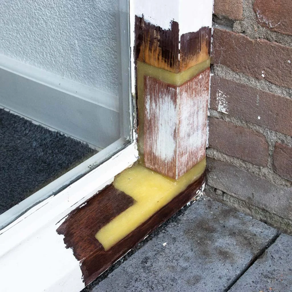 Onderkant van een kozijnstijl hersteld met een ingezet stuk hout en gele epoxy in Castricum