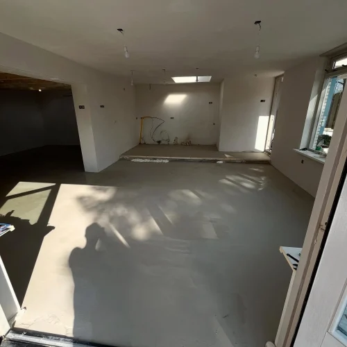 Geëgaliseerde vloer in een lege woonkamer met gestucte wanden, gezien vanuit de tuindeur in Castricum
