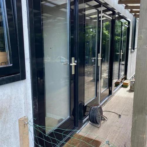 Hoogglans donker gelakte deuren en kozijnen langs een houten vlonder in Castricum
